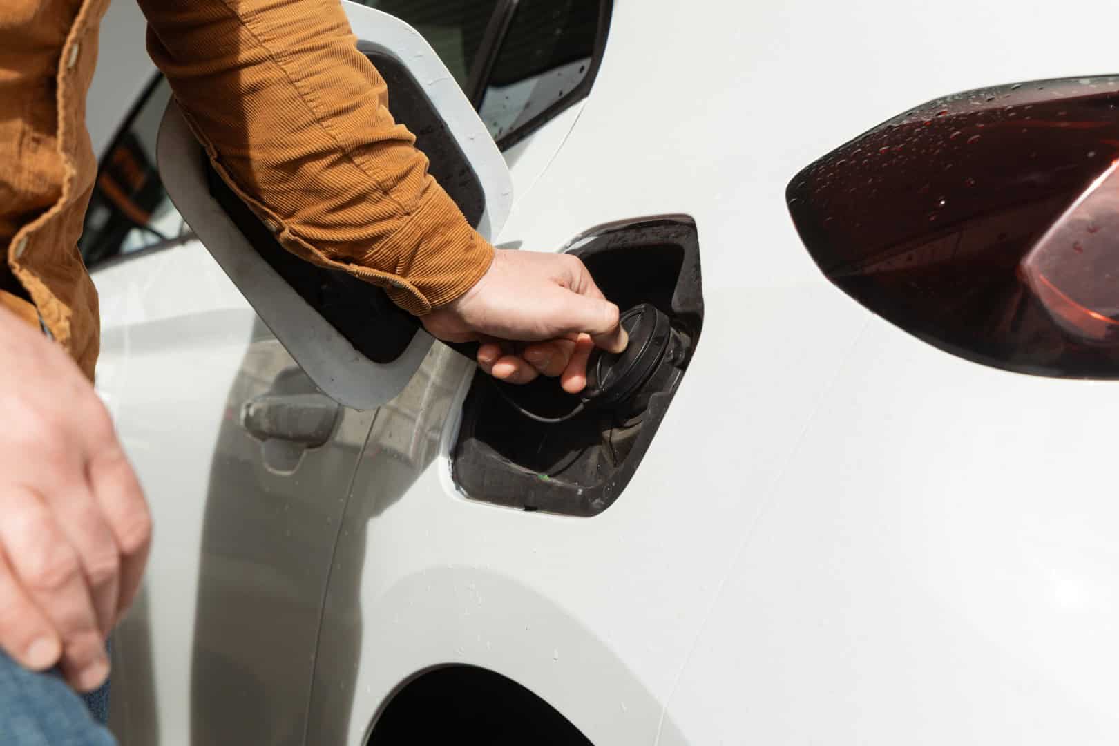 Individual is refueling vehicle at gas station with fuel nozzle in hand and car details visible